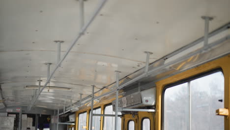 upward interior view on moving bus shows ceiling rails, poles, yellow window frames, frosted glass, metal fixtures, winter city sliding past outside, calm urban commute mood with soft daylight