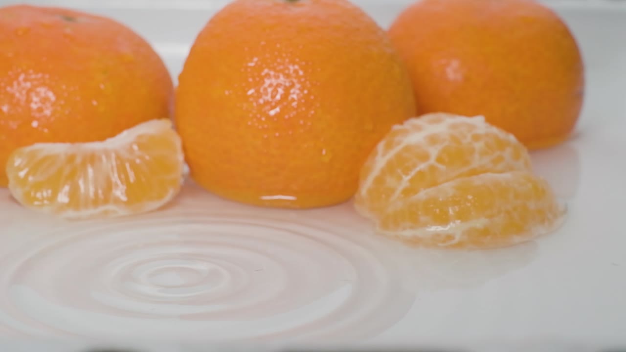 Tangkapan sangat dekat Potongan Jeruk Mandarin jatuh ke permukaan air, Gerakan lambat - Konsep Buah
