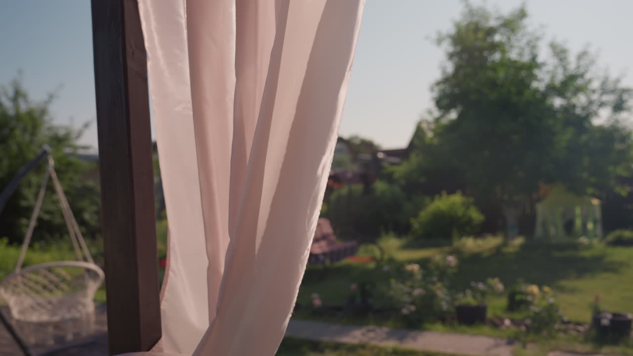 Tenda illuminata dal sole che ondeggia, il vento del mattino solleva il tessuto leggero, la luce del sole agita la tenda mentre il vento del mattino invita alla serenità, paesaggio distante incorniciato delicatamente dalla brezza e dalla luce del sole che danza sul tessuto