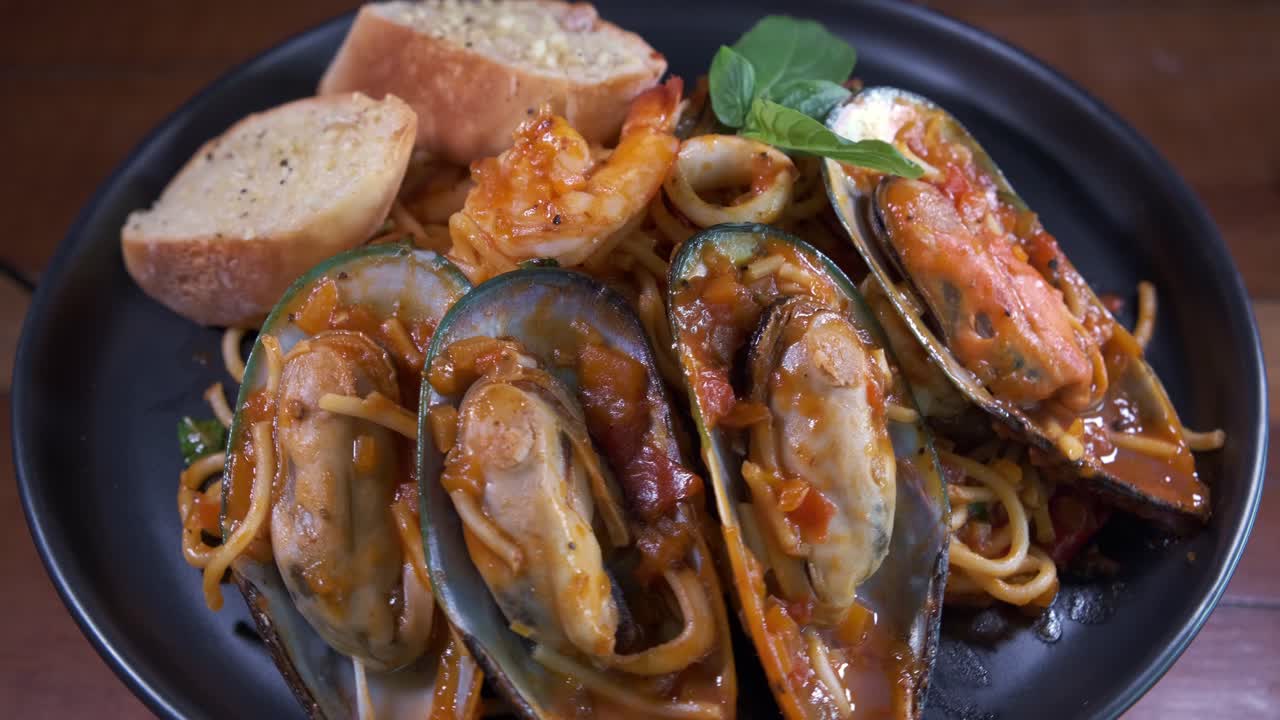 deliciosos mejillones de marisco con espagueti y pan de ajo girando en un plato negro