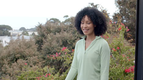 biracial woman smiling in front of lush garden with vibrant flowers, copy space