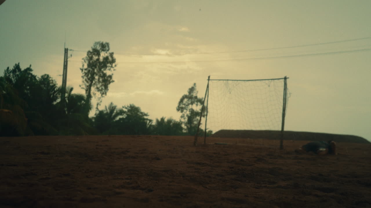 Young men playing football on a beach with stormy skies, slow-motion penalty shot
