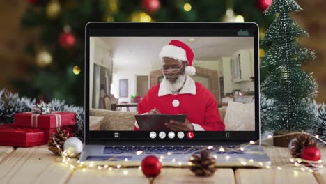 Älterer-Afroamerikanischer-Mann-Im-Weihnachtsmannkostüm-Bei-Videoanruf-Auf-Laptop,-Mit-Weihnachtsbaum