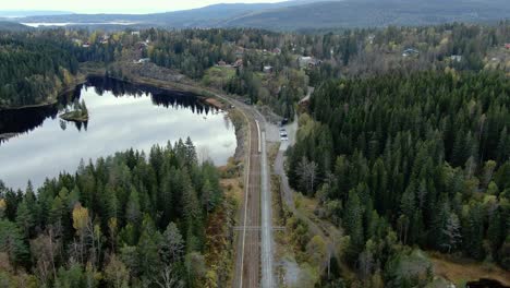 Vista-Aérea-De-Las-Vías-Del-Tren-Y-El-Lago-En-Las-Montañas-Con-árboles