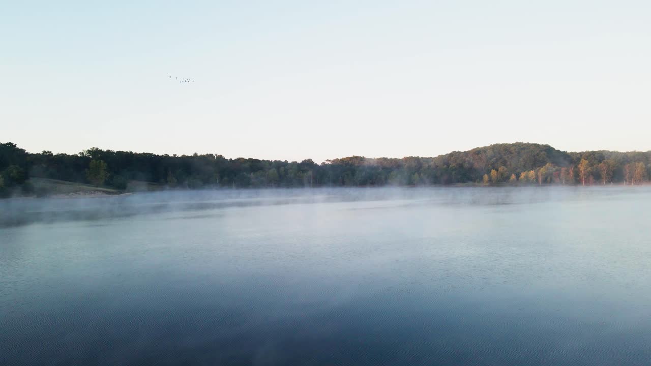 안개가 따뜻한 물에서 올라올 때 잔잔한 물이 유리처럼 앉아 있습니다.