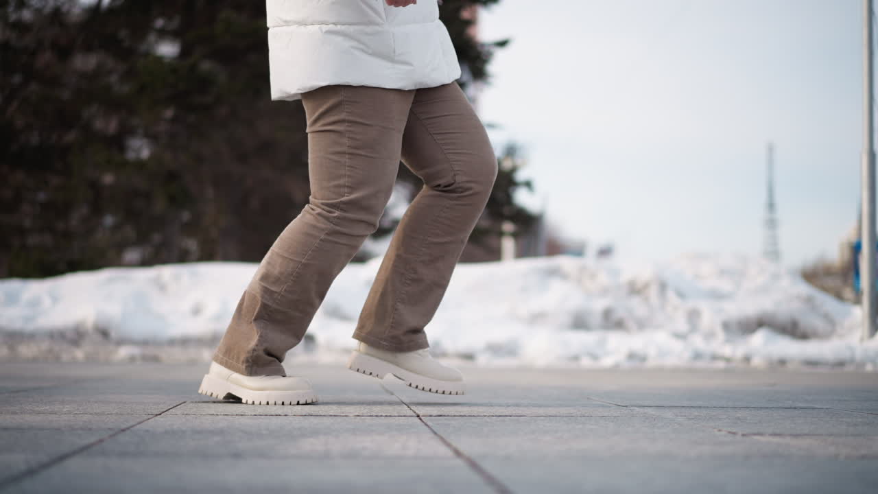 Girl dancing ballet outside busy snowy street, extending leg gracefully in corduroy pants and canvas boots against urban winter backdrop with pedestrians passing by and sunlight reflecting off snow