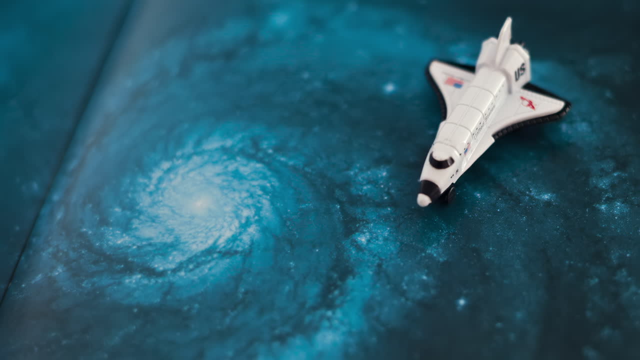 Close up of a miniature toy space shuttle placed on a blue cosmic galaxy backdrop