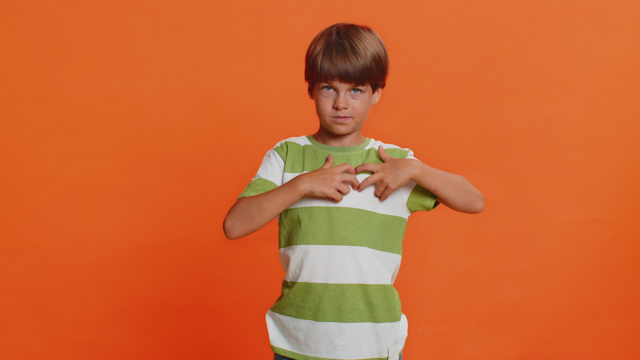 Smiling child boy makes heart gesture demonstrates love sign expresses good feelings and sympathy