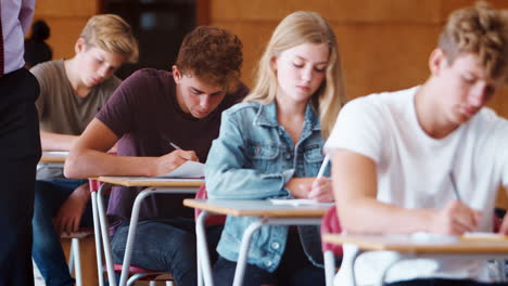 teenage students sitting examination with teacher invigilating