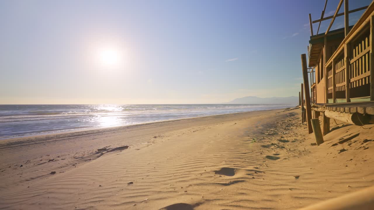 Praia deserta com céu limpo, perto de um restaurante de madeira.