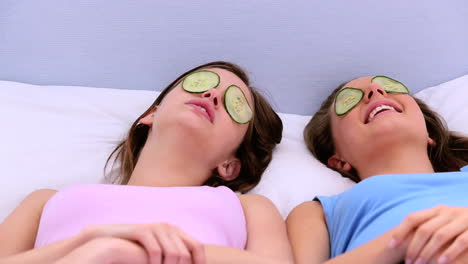 girls lying on bed with cucumber over their eyes