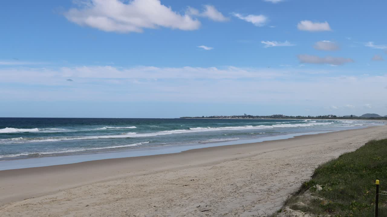 A tranquil beach scene with waves and shifting clouds.