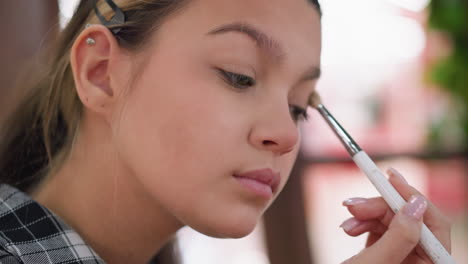 close-up of pretty young girl applying makeup on her eyes with a brush, she gently applies eye shadow to her eyelid, enhancing eye features and adding a finishing touch to her makeup routine