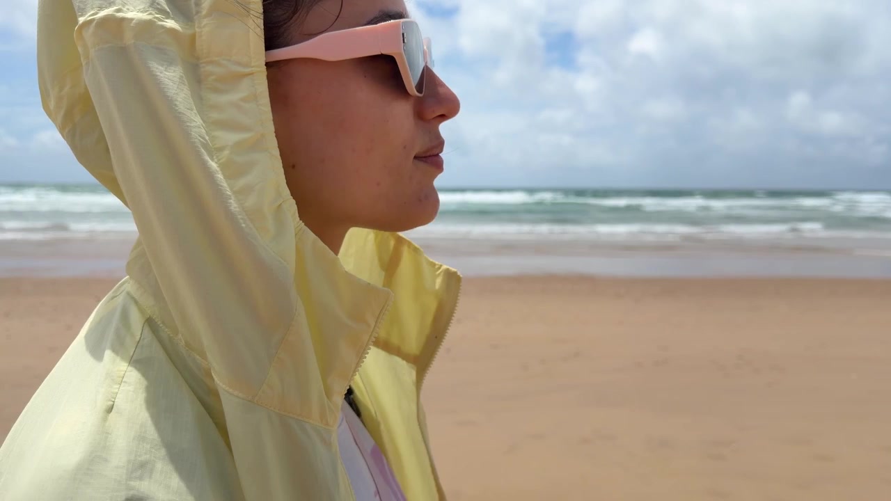 Young Woman Wearing Yellow Hooded Jacket Standing on Sandy Beach