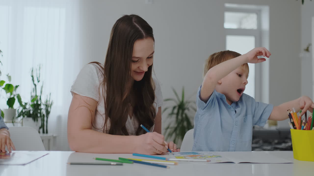 una familia de dos niños y una joven madre sentada en la mesa dibuja en papel con lápices de colores. desarrollo de la creatividad en los niños.