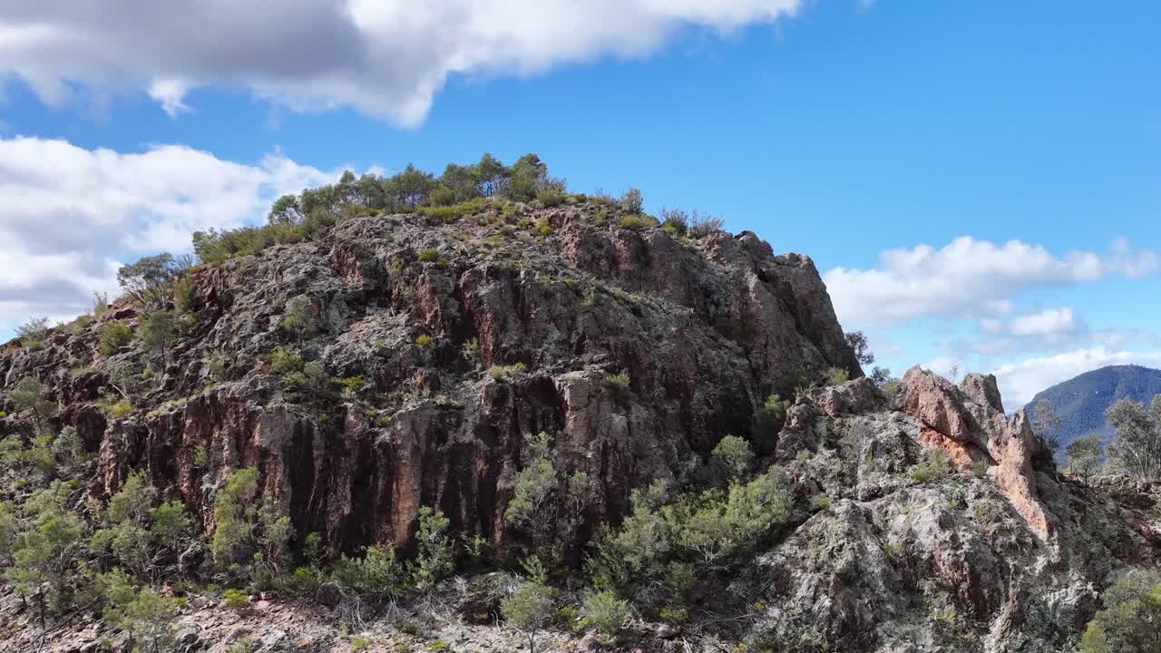 Drone camera smoothly pans across rugged Split Rock, revealing dramatic cliffs, sparse vegetation, and expansive blue sky in bright daylight