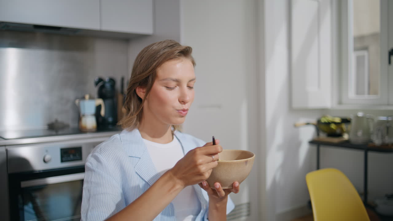 Closeup woman eating breakfast in kitchen sunlight. Content woman enjoying food