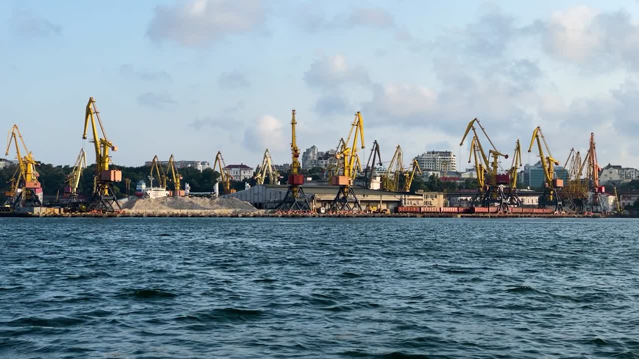 grúas de doble pluma en el puerto de odesa con un montón de arena de un barco que navega en el mar negro
