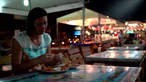 una mujer está mojando un camarón en una salsa y comiendo. comida callejera