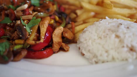 a plate of chicken stir-fry with rice and french fries