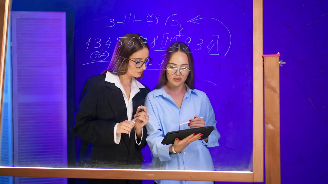 Women in business strategy. Two women engage in a strategy session, discussing plans and making notes on a glass board
