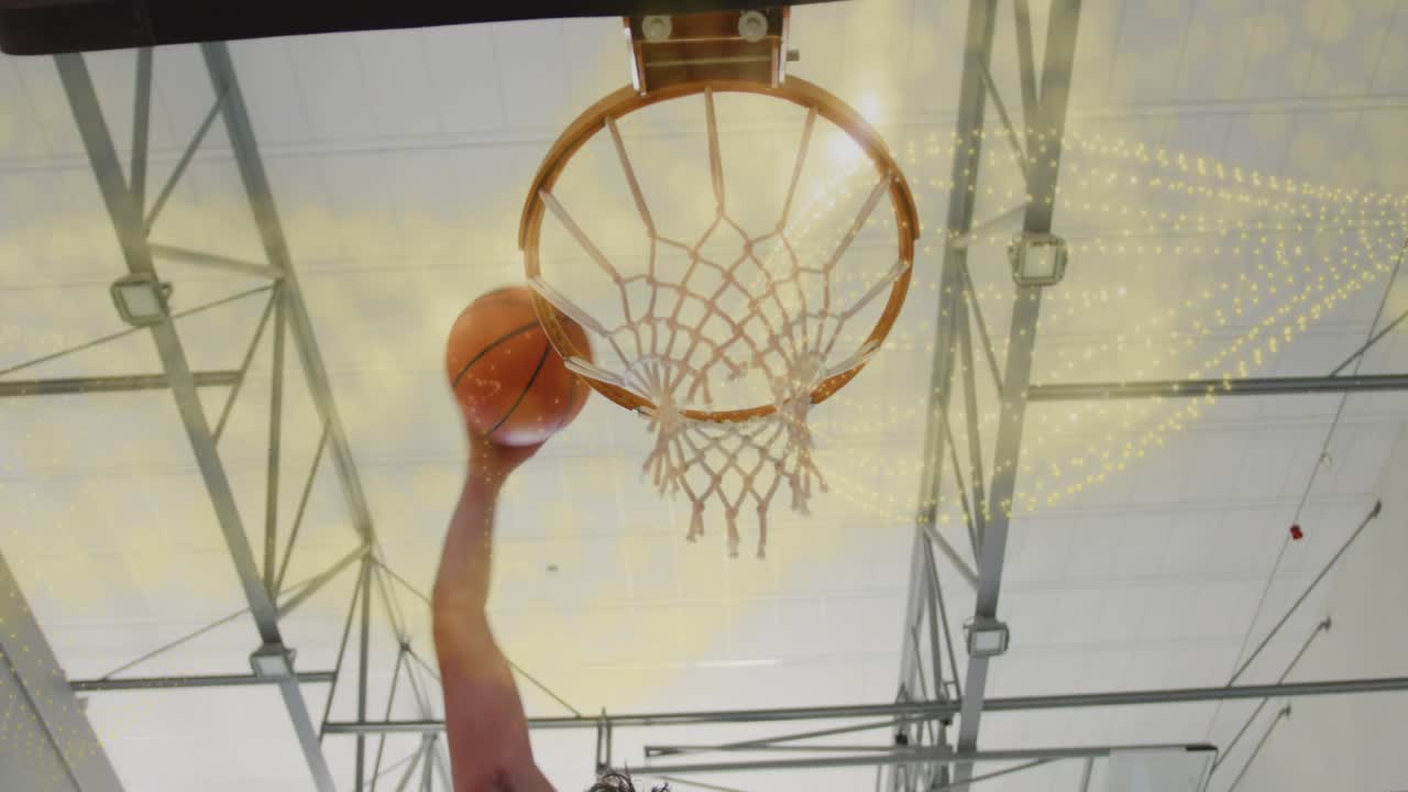 Atleta uomo che spinge il pallone da basket verso l'alto durante una sessione in palestra, mandando la palla attraverso il canestro e facendo increspare la retina.