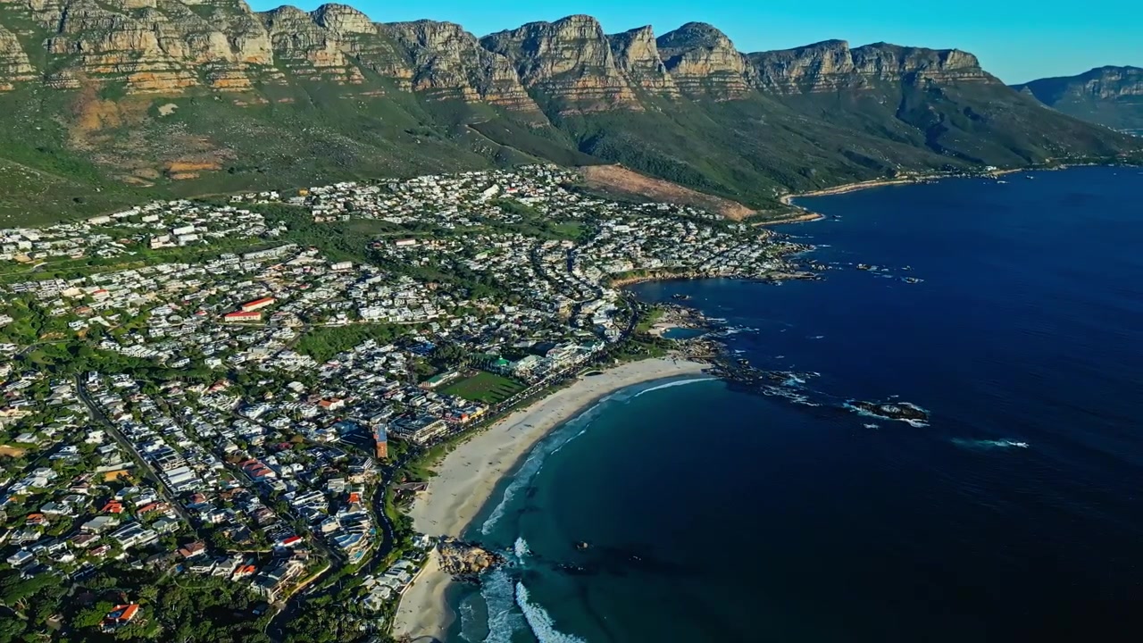 Camps Bay ve Cape Town, Güney Afrika, Atlantik kıyı şeridinin üzerinde yükselen Masa Dağı, plajlar ve sahil manzarası, sinematik havadan görünüm.