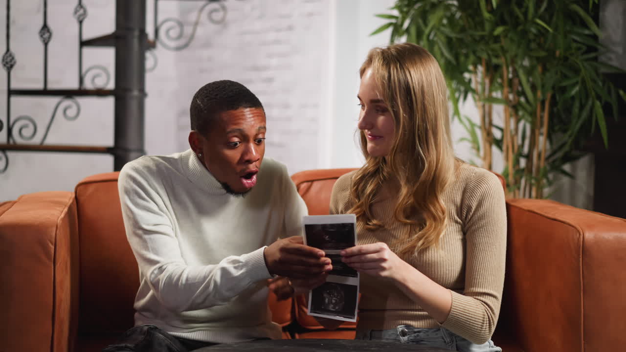 la esposa blanca muestra imágenes de ultrasonido al hombre negro en casa