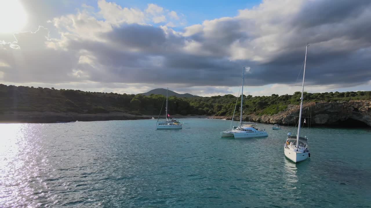 Experience the tranquil beauty of Cala Varques in Majorca, where sailboats anchor amidst crystal-clear waters and scenic cliffs, perfect for relaxation and exploration on a sunny day.