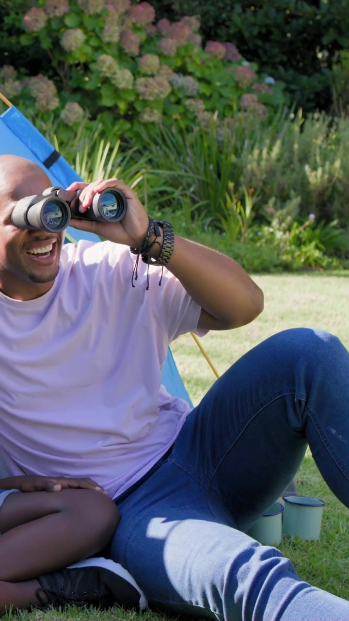 Vertical video: Reaching binoculars father in pink tee scanning garden, guiding binoculars to child
