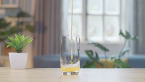 orange juice being poured into a glass on the table at home