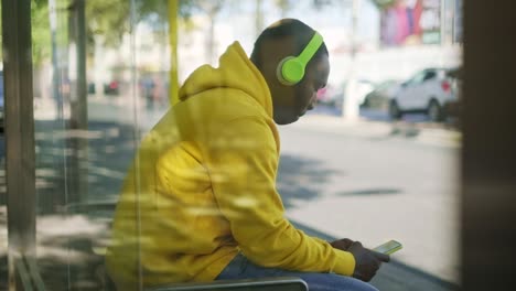 african young man listening to music at bus stop