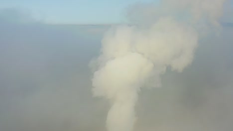 smoke from a power station chimney rising from a low, creeping fog. drone view