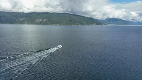 High-angle-panoramic-view-of-tourist-boat-crossing-Sognefjord-Norway---Aerial-starting-wat-distant-with-mountain-and-scenery-background-before-slowly-approaching-boat