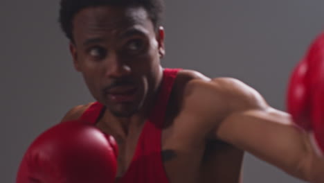 Close-Up-Studio-Shot-Of-Male-Boxer-Wearing-Boxing-Gloves-In-Boxing-Match-Throwing-Punches-Against-Grey-Background