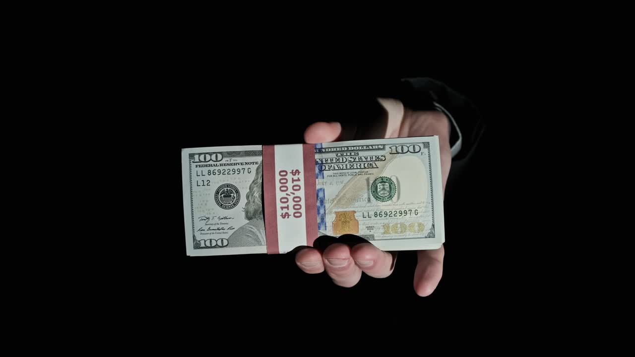 Stak af 10.000 amerikanske dollars i en bundt i mandlige hænder på sort baggrund.