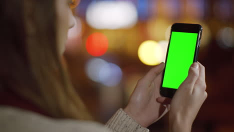 las manos de la chica desplazándose simulando el teléfono al aire libre. la mujer mirando el teléfono pantalla verde.