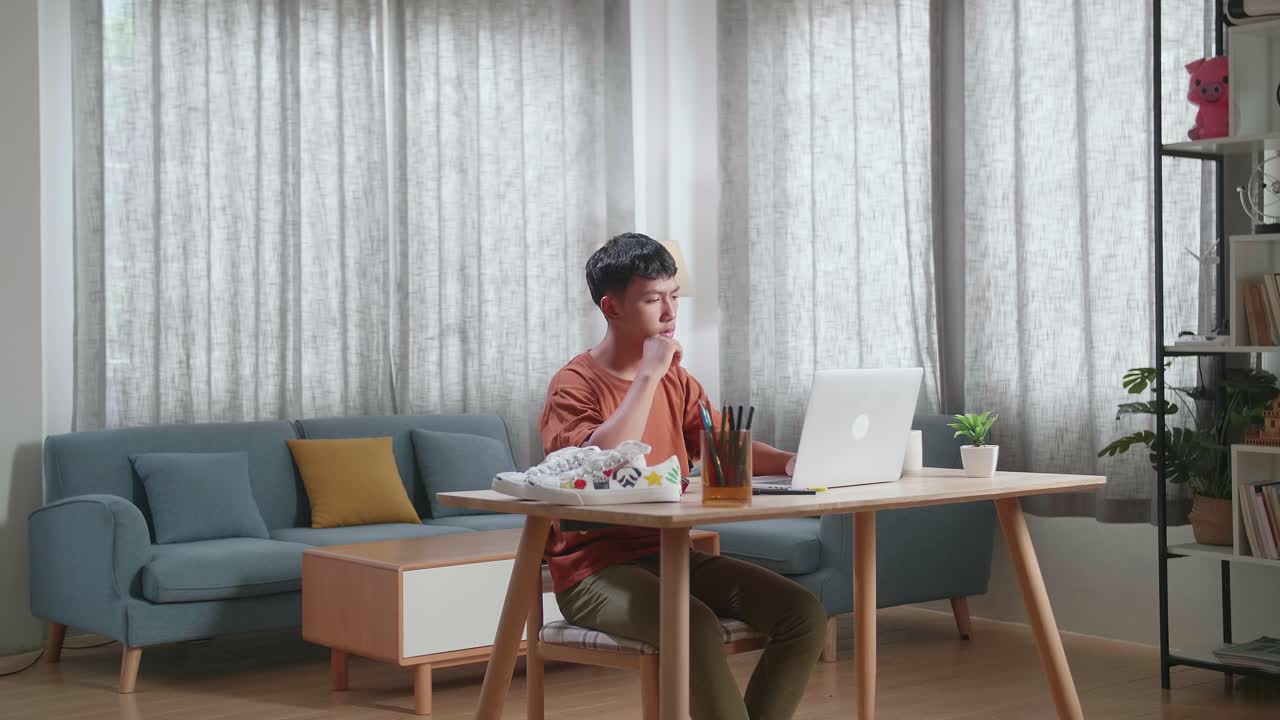 아시안 소년 신발 디자이너가 생각하고 집에서 노트북을 사용하면서 지표손가락을 올리고 있습니다.