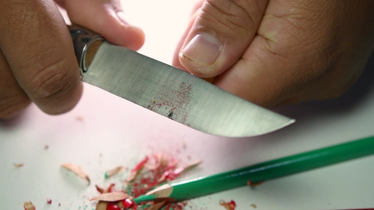 날카로운 칼로 연필과 색연필을 천천히 갈고 있는 손의 영상