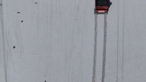 An-aerial,-top-down-view-of-an-orange-tractor-raking-an-empty-beach-on-a-sunny-day