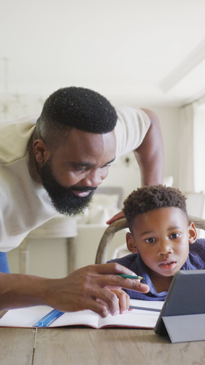 Video verticale di padre e figlio afroamericani che fanno i compiti insieme, al rallentatore