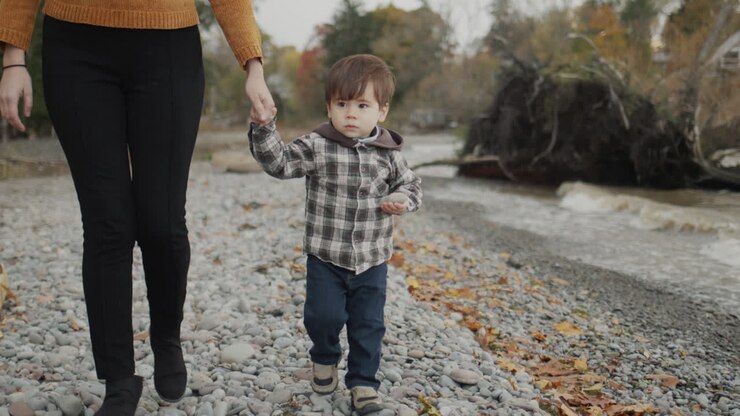 A young woman leads a boy by the hands along the rocky seashore