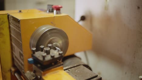 Close-up-of-old-dusty-Turning-lathe-in-action,-cutting-off-a-layer-of-a-metal-bar-in-old-workshop