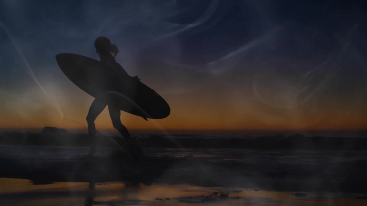 Surfista che emerge dalla riva camminando sulla sabbia bagnata al tramonto, con nebbia vorticante, per una promozione di surf.