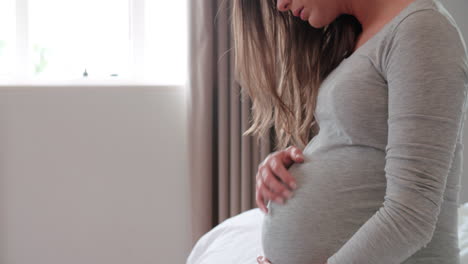 depressed pregnant woman sitting on bed holding belly