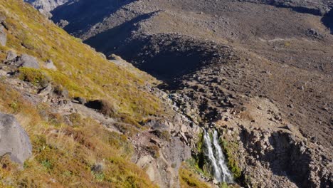 la cascada drena una alta meseta volcánica con hierba y roca.