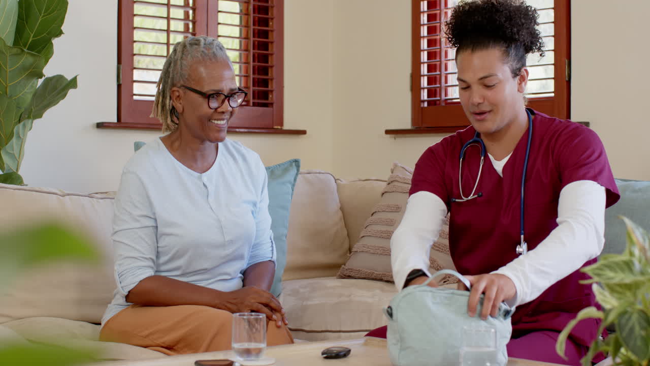 Senior woman receiving medication from caregiver at home, smiling and relaxed
