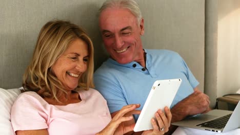 pareja sonriente acostada en la cama y usando una tableta digital