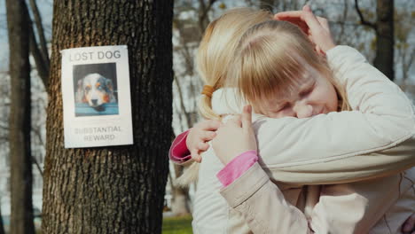 mom soothes the girl who lost the dog on the tree hangs the announcement of the missing puppy