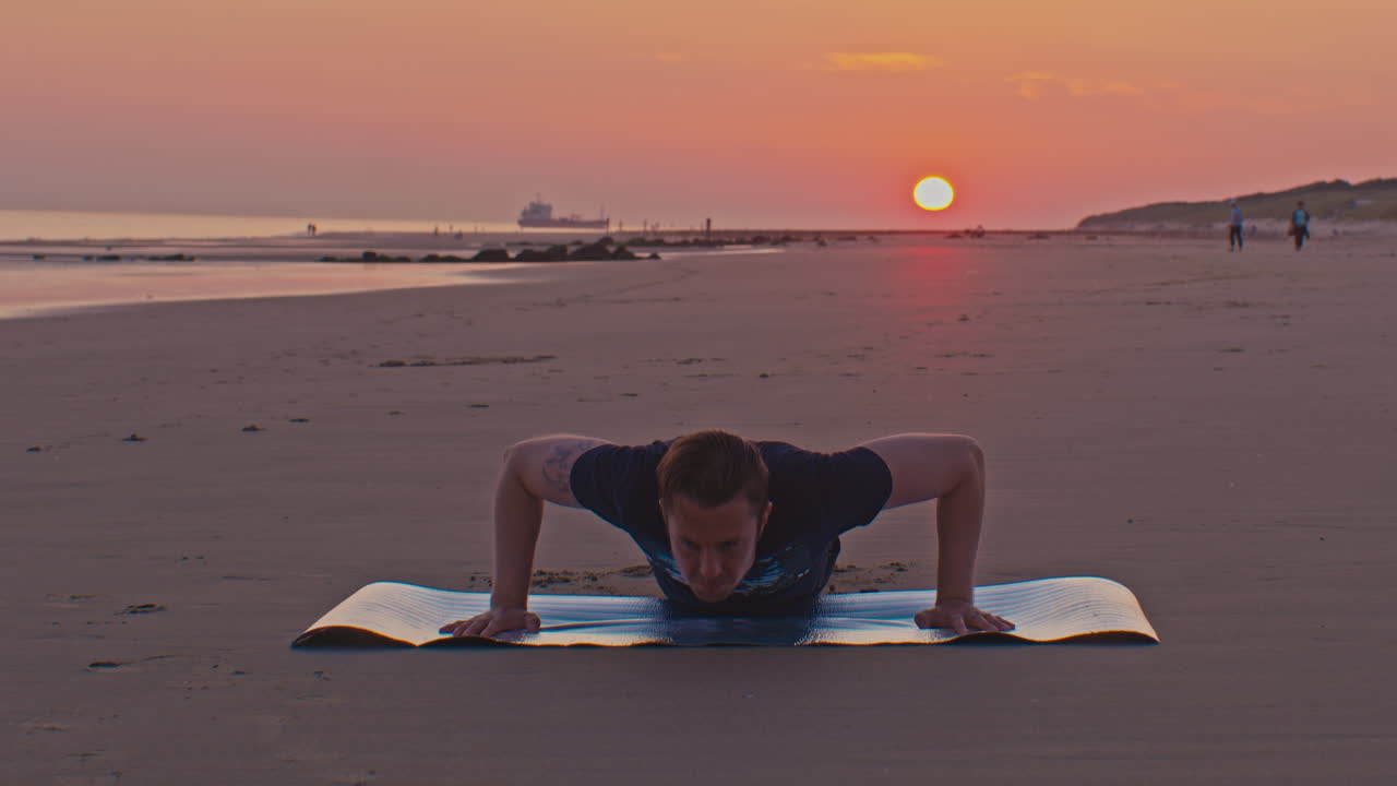 Modello maschile olandese, caucasico, europeo, snello, bianco, si allena al tramonto facendo flessioni sulla sabbia della spiaggia nel Mare del Nord dei Paesi Bassi con il sole che tramonta sullo sfondo